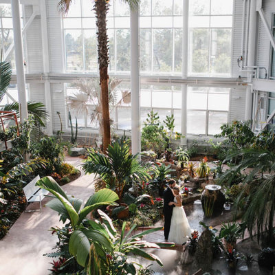 A bride and groom pose together in a sunny conservatort.