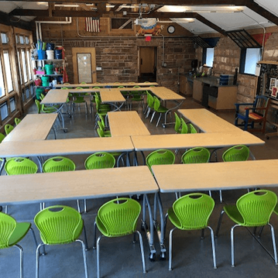 Bright green chairs are pushed in around several brown tables, inside an empty classroom.