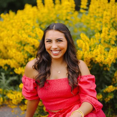 Rebekah in a pink dress sitting in front of flowers.
