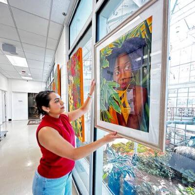 Artist Rebekah Entz is hanging one of her portraits in the window of the Gardens.