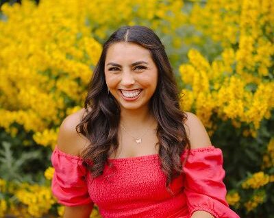 Rebekah in a pink dress sitting in front of flowers.