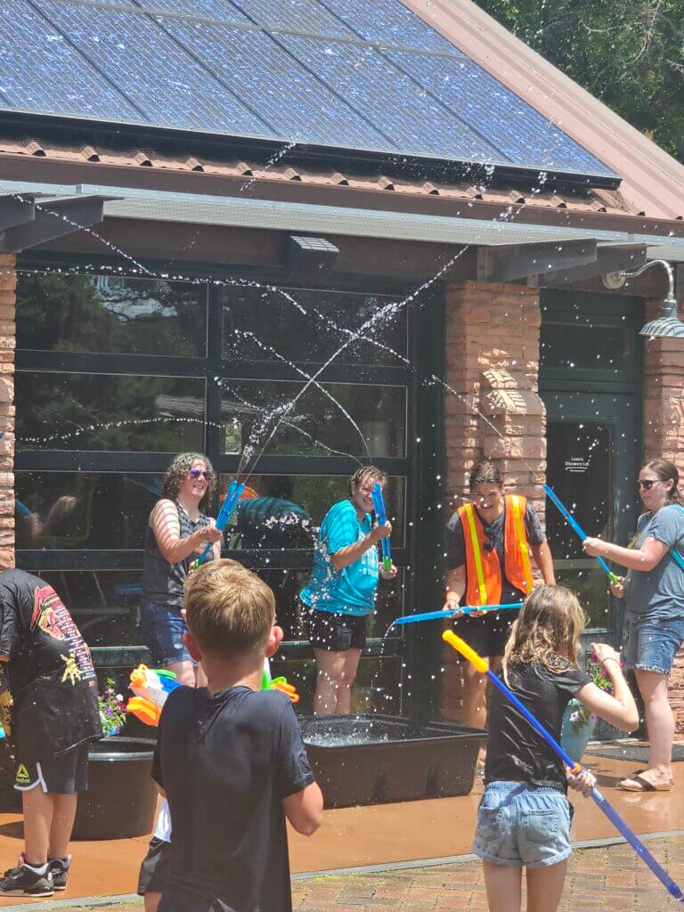 Children and adults participate in an outdoor water fight. Streams of water arc through the air. — Story Time