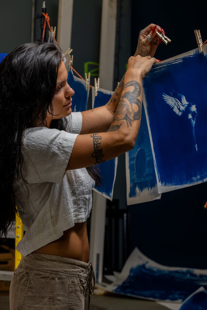  CariFaye hanging fabric cyanotypes on a line with clothes pins.