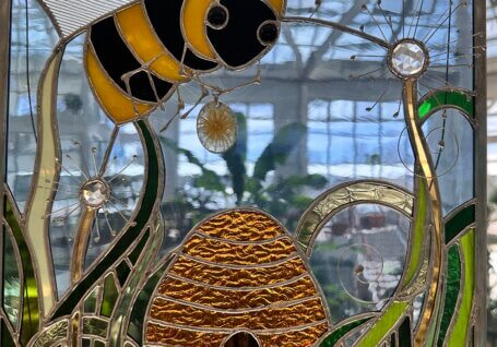 Glass art window piece of a bee, grass and a bee hive.